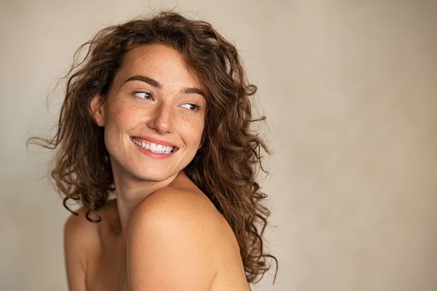 Portrait de femme à la peau tâcheté aux cheveux chatains bouclés regardant vers l&apos;arrière et au épaules dénudés