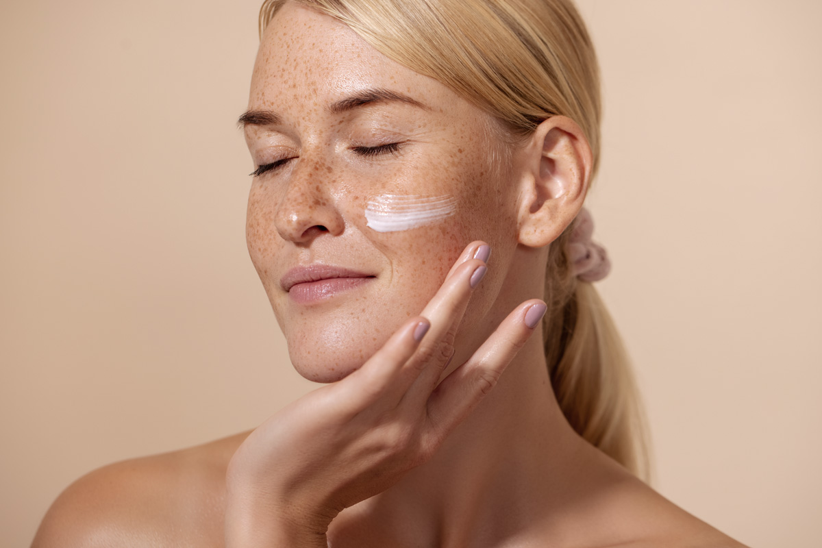 Portrait d'une jeune femme appliquant de la crème sur ça joue droite.