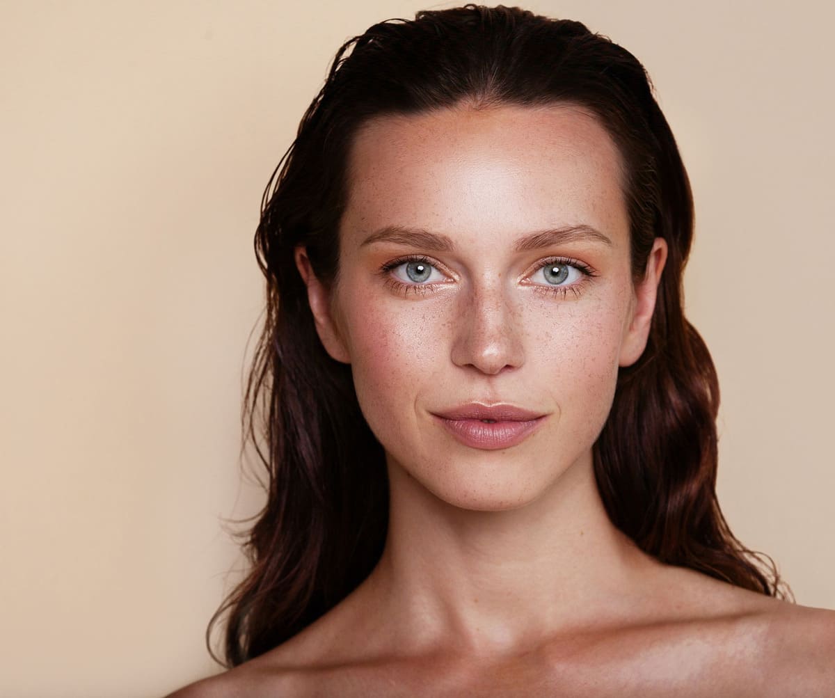 Portrait d'une jolie jeune femme aux cheveux frisés brun foncé sur fond beige brun pâle.