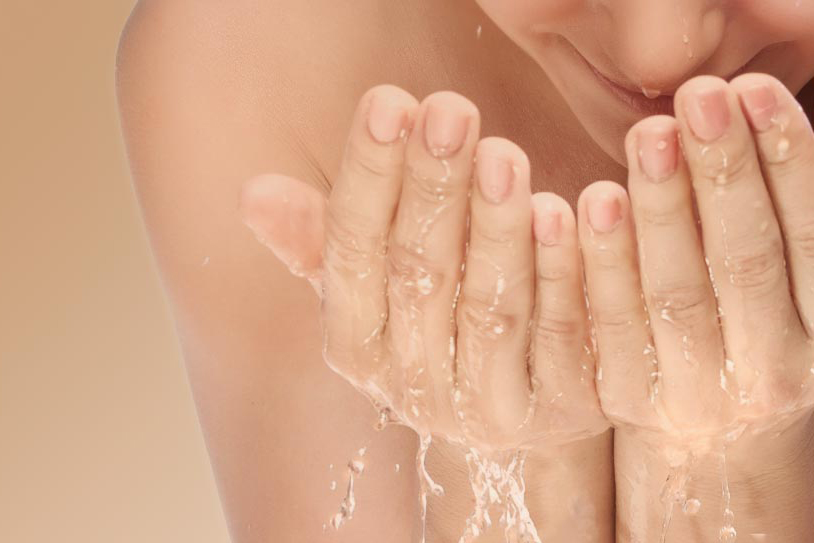 Image d'une femme qui se rince le visage avec de l'eau avec ses mains.